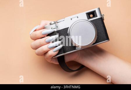 Main de femme avec un vernis à ongles gris tenant un appareil photo Banque D'Images