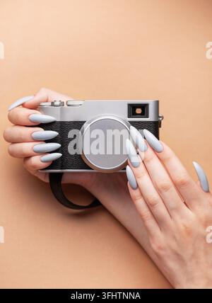 Main de femme avec un vernis à ongles gris tenant un appareil photo Banque D'Images