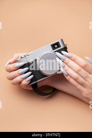 Main de femme avec un vernis à ongles gris tenant un appareil photo Banque D'Images