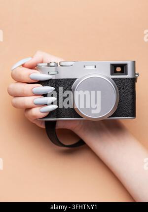 Main de femme avec un vernis à ongles gris tenant un appareil photo Banque D'Images