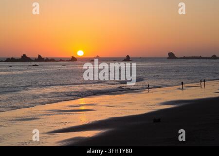 Coucher de soleil, vue sur la côte nord du Pacifique, marée basse, îles rocheuses, personnes marchant sur la plage. Oiseaux en vol. Banque D'Images