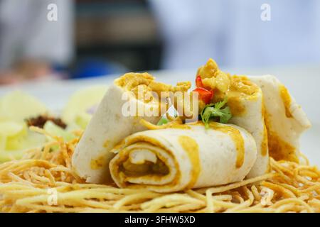 Tranches de wrap au poulet au curry servies sur des nouilles frites croustillantes Banque D'Images