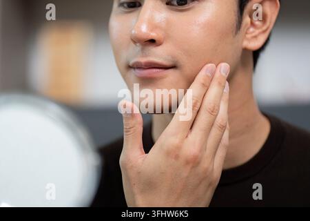 Routine de soin de la peau. Jeune homme appliquant la crème hydratante devant le miroir. Banque D'Images