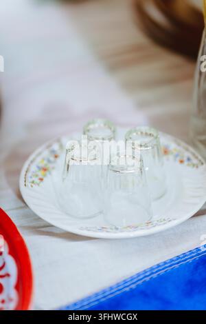 Gros plan de quatre petits verres transparents posés à l'envers sur une soucoupe en céramique blanche décorée d'un délicat motif floral coloré sur le bord. Banque D'Images