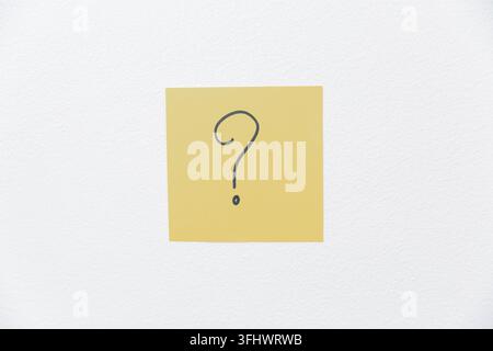 Post-it jaune avec un point d'interrogation dessiné à la main centré sur un fond blanc propre, représentant des questions, de l'incertitude, de la curiosité, la résolution de problème Banque D'Images