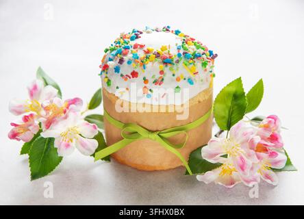 Délicieux gâteau de Pâques décoré de paillettes colorées et noué avec un ruban vert près de fleurs en fleurs Banque D'Images
