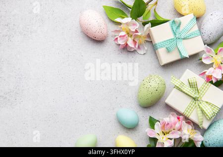 Les œufs de pâques colorés et les boîtes-cadeaux reposent sur un fond gris décoré de fleurs printanières Banque D'Images