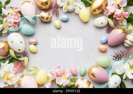 Cadre d'oeufs de Pâques formant un cercle sur un fond gris avec des fleurs et des plumes, créant un espace de copie au centre Banque D'Images