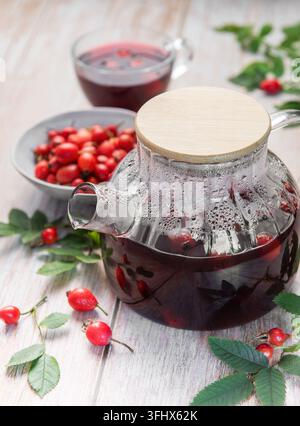Thé à la rose musquée fumant dans une théière en verre avec des rose musquée fraîches Banque D'Images