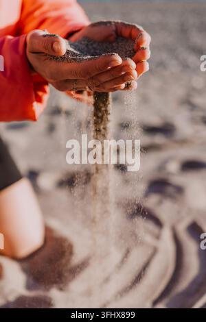 Mains laissant couler du sable entre les doigts sur une plage ensoleillée représentant le concept du temps qui passe et de l'éternité Banque D'Images