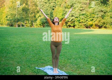 Jolie femme debout dans un parc naturel printanier les bras grands ouverts levés vers le haut Banque D'Images