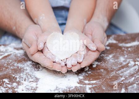 Vue du dessus père et main de l'enfant, découper des biscuits en forme de cœur dans la pâte Banque D'Images