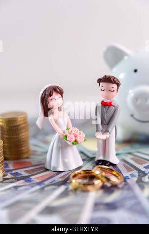 Figurines de mariée et marié debout sur des billets avec des alliances au premier plan, représentant le financement du mariage, les dépenses de mariage, le budget et Banque D'Images