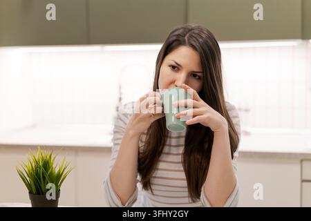 Une femme boit du café dans une tasse verte Banque D'Images