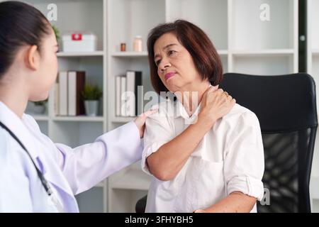 Une infirmière offre réconfort et conseils médicaux à une femme âgée souffrant de douleurs à l’épaule. L'empathie et les soins centrés sur le patient. Banque D'Images