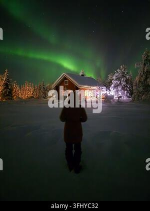 Un spectacle fascinant de aurores boréales danse dans le ciel nocturne à Akaslompolo, en Laponie. Un personnage se tient en admiration, entouré d'un merveilleux lan hivernal Banque D'Images