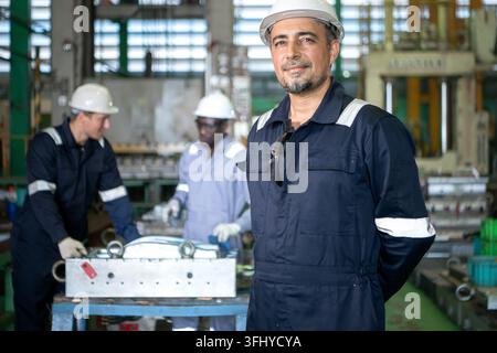 Chef d'équipe industriel debout dans une usine de fabrication avec des ouvriers opérant des machines en arrière-plan, représentant le travail d'équipe et la relations publiques industrielles Banque D'Images