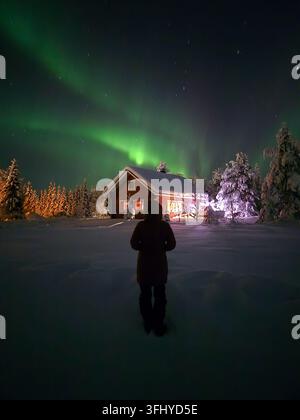 Un spectacle à couper le souffle des aurores boréales danse dans le ciel d'hiver au-dessus d'une charmante cabane à Akaslompolo, en Laponie. Banque D'Images