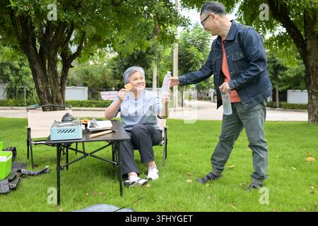 Couple senior appréciant la nourriture pendant le camping dans un parc, créant une atmosphère détendue et conviviale de style de vie en plein air Banque D'Images