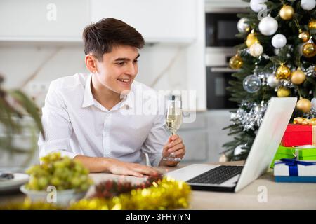 Un homme élégamment habillé communique joyeusement avec ses proches par appel vidéo le soir du Nouvel An Banque D'Images