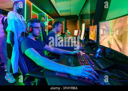 Les joueurs compétitifs se concentrent dans un centre LAN éclairé au néon, portant des casques et utilisant des claviers et des moniteurs RVB pendant une session FPS multijoueur, créat Banque D'Images