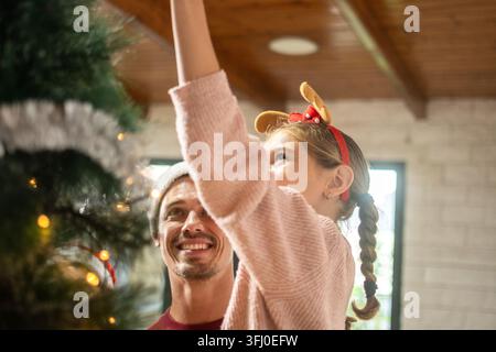 Père et fille décorant ensemble le sapin de Noël à la maison Banque D'Images