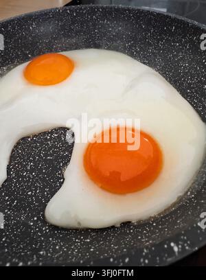 Œuf au plat avec deux jaunes orangés cuisant dans une poêle antiadhésive tachetée Banque D'Images