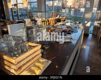Un espace petit-déjeuner en libre-service organisé avec des verres à boisson et des collations saines disposés sur une table élégante dans une salle à manger baignée de soleil, évoquant une prof... Banque D'Images