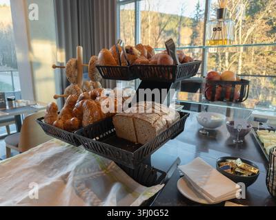 Pain artisanal et croissants dorés servis sur un présentoir moderne à plusieurs niveaux dans un restaurant lumineux, représentant un petit-déjeuner gourmet sain Banque D'Images