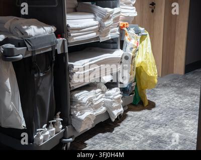 Le chariot d'hôtel contient des serviettes soigneusement empilées, des draps pliés et des accessoires en papier pour le travail d'entretien quotidien, représentant l'efficacité au sein du p Banque D'Images