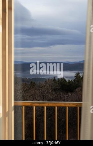 La vallée brumeuse et les collines lointaines vues depuis un balcon en bois rustique offrent une perspective tranquille de la nature, parfaite pour mettre en valeur un tourisme calme ou un Banque D'Images