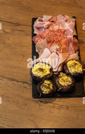 Plateau de charcuterie avec viandes séchées, fromages variés, raisins, noix et champignons farcis au fromage, mettant en valeur des hors-d'œuvre gastronomiques et un service de traiteur pour fêtes Banque D'Images