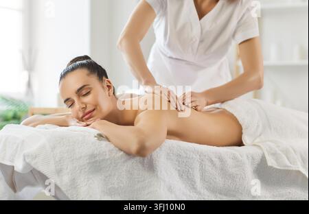 Jeune femme souriante les yeux fermés profitant d’un massage relaxant du dos dans un centre de spa bien-être. Banque D'Images