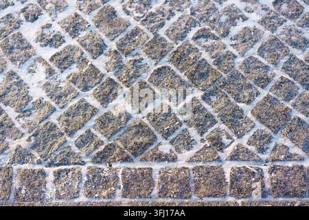 Ancien motif de pavage en pavés gris bruns, rue vue par le dessus avec des lignes de joints blanches Banque D'Images