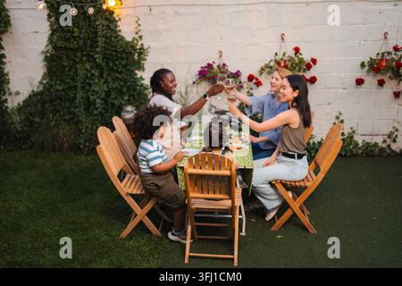 Famille et amis divers souriant et grillant des boissons lors d'un dîner festif en plein air Banque D'Images