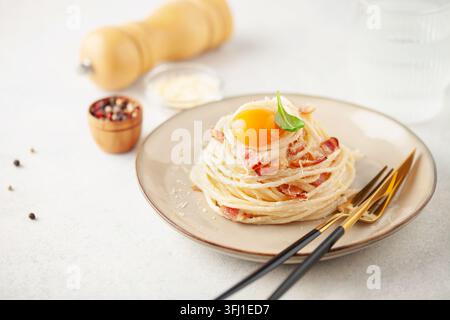 Spaghetti carbonara - pâtes au bacon, sauce crémeuse, jaune d'œuf et parmesan râpé, garnies d'une feuille de basilic dans une assiette en céramique ronde Banque D'Images