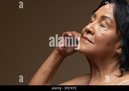 Femme afro-américaine âgée se penchant en arrière, yeux fermés sous un éclairage de studio, haut à bretelles, espace de copie Banque D'Images