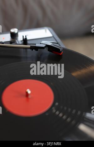 Disque vinyle noir tournant sur une platine avec bras de lecture abaissant la cartouche et pointe rouge Banque D'Images