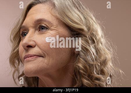 Femme âgée regardant légèrement vers le haut à gauche dans un portrait de studio avec une traînée de crème blanche sur la joue Banque D'Images