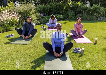 Divers amis dans l'équipement d'entraînement faisant l'étirement de papillon sur la pelouse herbeuse avec des tapis, des chaussures, des bouteilles. Yoga, plein air, groupe, fitness, bien-être, nature, gar Banque D'Images