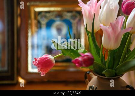 Tulipes roses et blanches dans un vase à côté d'une icône orthodoxe Banque D'Images