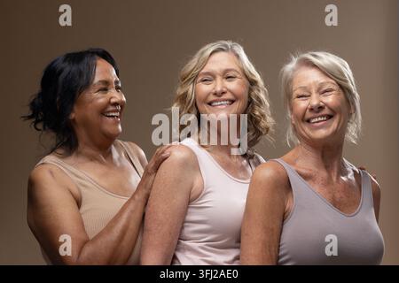 Amies âgées et matures posant en riant en studio, portant des débardeurs et des boucles d'oreilles Banque D'Images