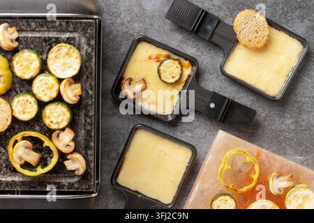 Délicieux fromage à raclette suisse fondu traditionnel sur des légumes cuits ou cuits en dés servis dans des poêles individuelles. Banque D'Images