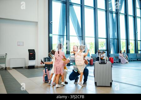 Père embrassant ses trois filles arrivant au guichet de l'aéroport Banque D'Images