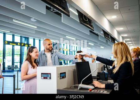Jeune couple qui termine le processus d'enregistrement à l'aéroport, reçoit la carte d'embarquement du personnel de la compagnie aérienne Banque D'Images
