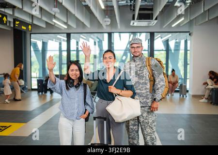 Famille heureuse faisant signe, debout avec des bagages à l'aéroport Banque D'Images
