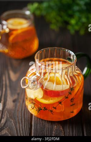 Théière en verre avec thé chaud aux agrumes à partir d'oranges, citrons, pommes, mandarines et thym. Boisson saine sur fond de bois sombre Banque D'Images
