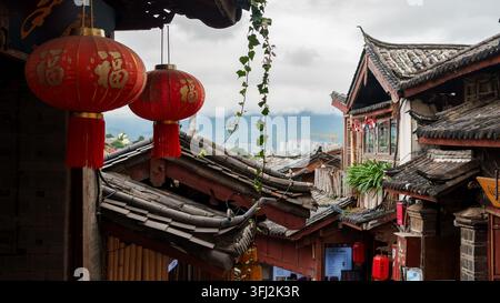 Lanternes rouges suspendues au-dessus des toits traditionnels en tuiles de la vieille ville de Lijiang, Yunnan, Chine Banque D'Images