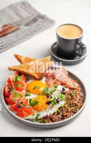 Petit déjeuner sain - œufs, pain grillé, sarrasin, bacon, haricots et tomates sur une assiette sur la table. Banque D'Images