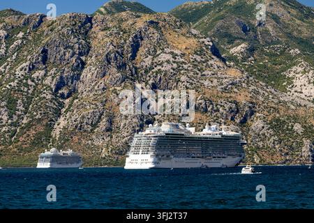 4 juillet 2026, Kotor, Monténégro, un navire de croisière passe devant des formations rocheuses escarpées et des falaises vertes abruptes, avec une eau bleu profond et calme, une lumière solaire vive réfléchie Banque D'Images